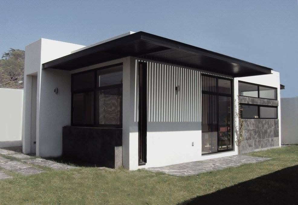 Fachada de casa de una planta con celosías verticales y pérgola negra