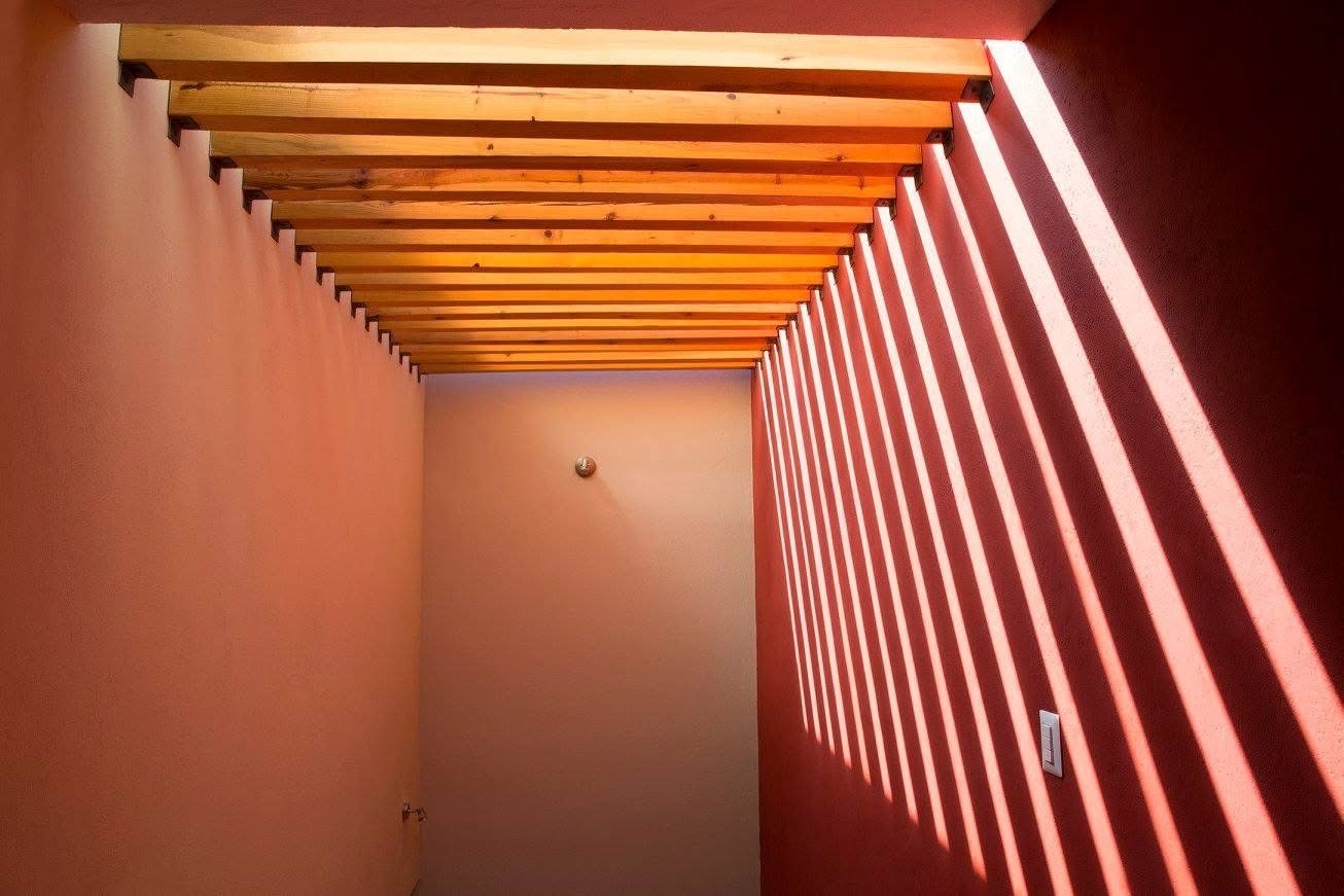 Vigas de madera y luz cenital proyectando líneas sobre muro coral